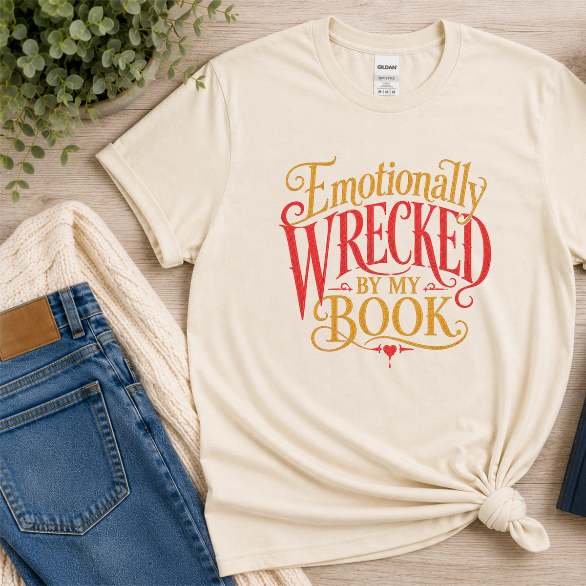 Natural cream T-shirt laid flat with ornate red and gold lettering and the words “Emotionally Wrecked by My Book.”