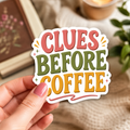 Hand holding a white-bordered sticker reading “Clues Before Coffee,” featuring coral, olive, and gold block lettering with small sparkles.