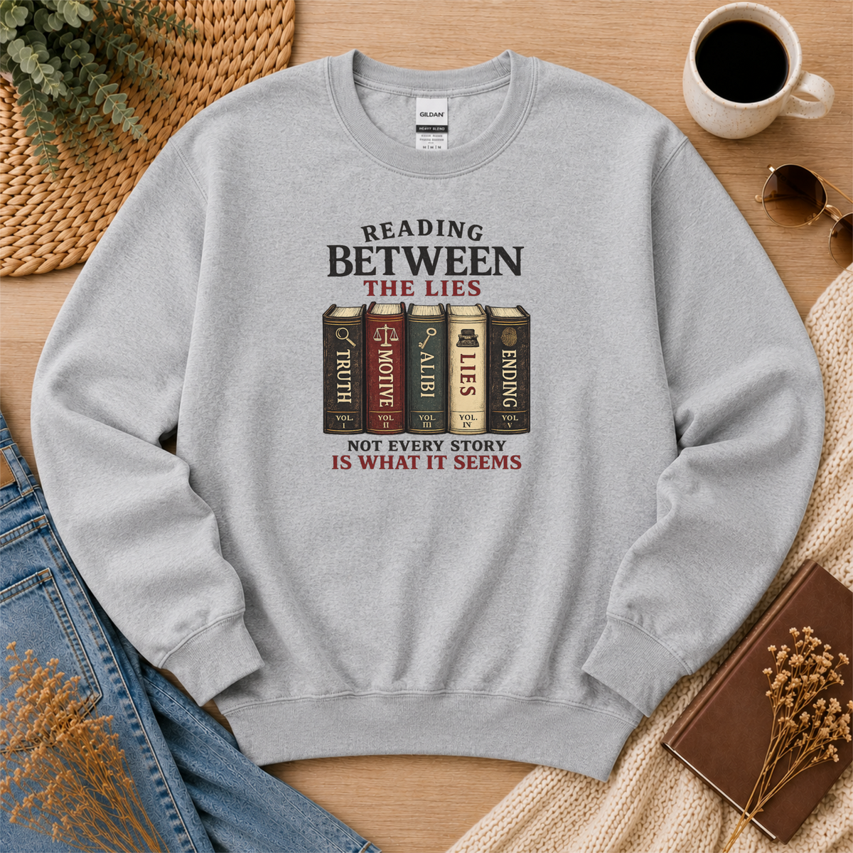 Sport gray crewneck sweatshirt laid flat with books labeled Truth, Motive, Alibi, Lies and Ending and the words “Reading Between the Lies. Not Every Story Is What It Seems.”