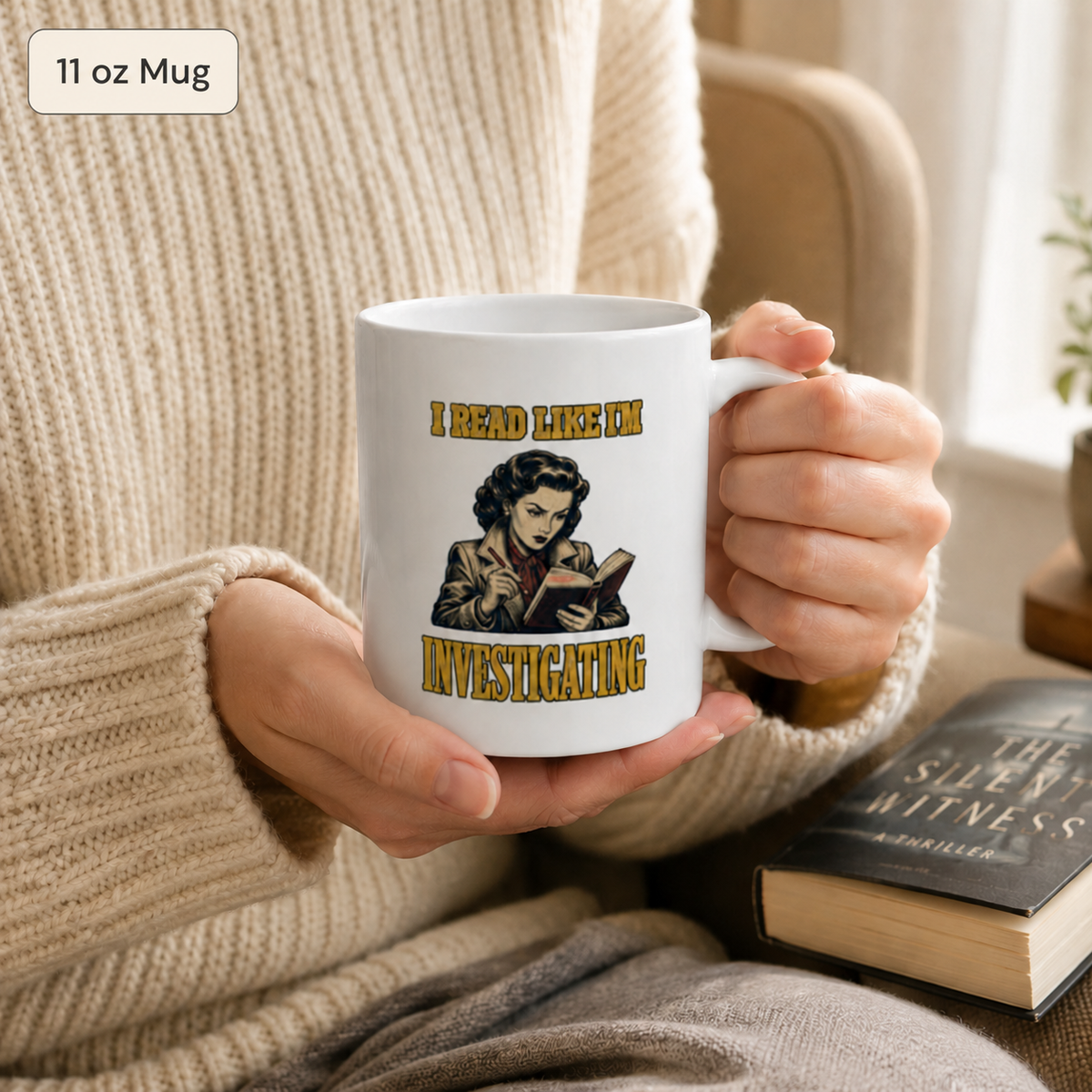 Person in a cream sweater holding the white 11 oz I Read Like I’m Investigating mug at a table with a book nearby.