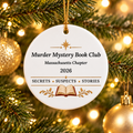 White round ornament on a lit tree, with gold accents and an open book; reads “Murder Mystery Book Club,” “Massachusetts Chapter,” “2026” and “Secrets • Suspects • Stories.”