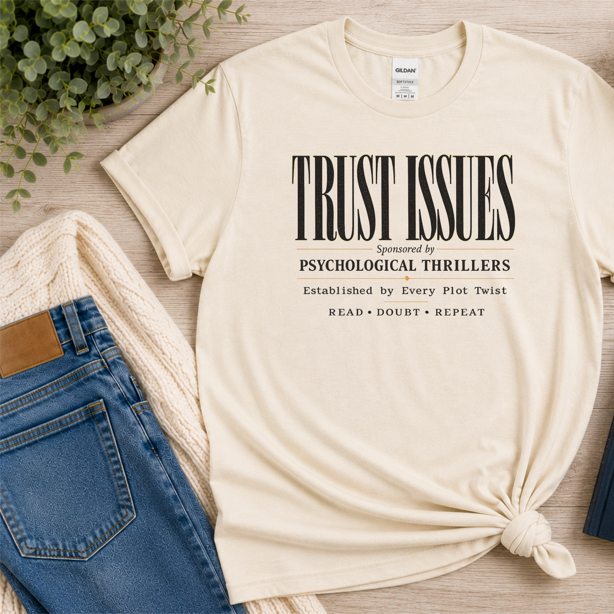 Natural cream T-shirt laid flat with stacked typography and the words “Trust Issues. Sponsored by Psychological Thrillers. Established by Every Plot Twist. Read Doubt Repeat.”
