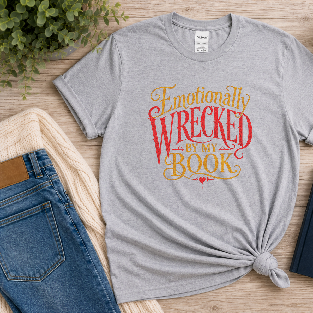 Sport gray T-shirt laid flat with ornate red and gold lettering and the words “Emotionally Wrecked by My Book.”