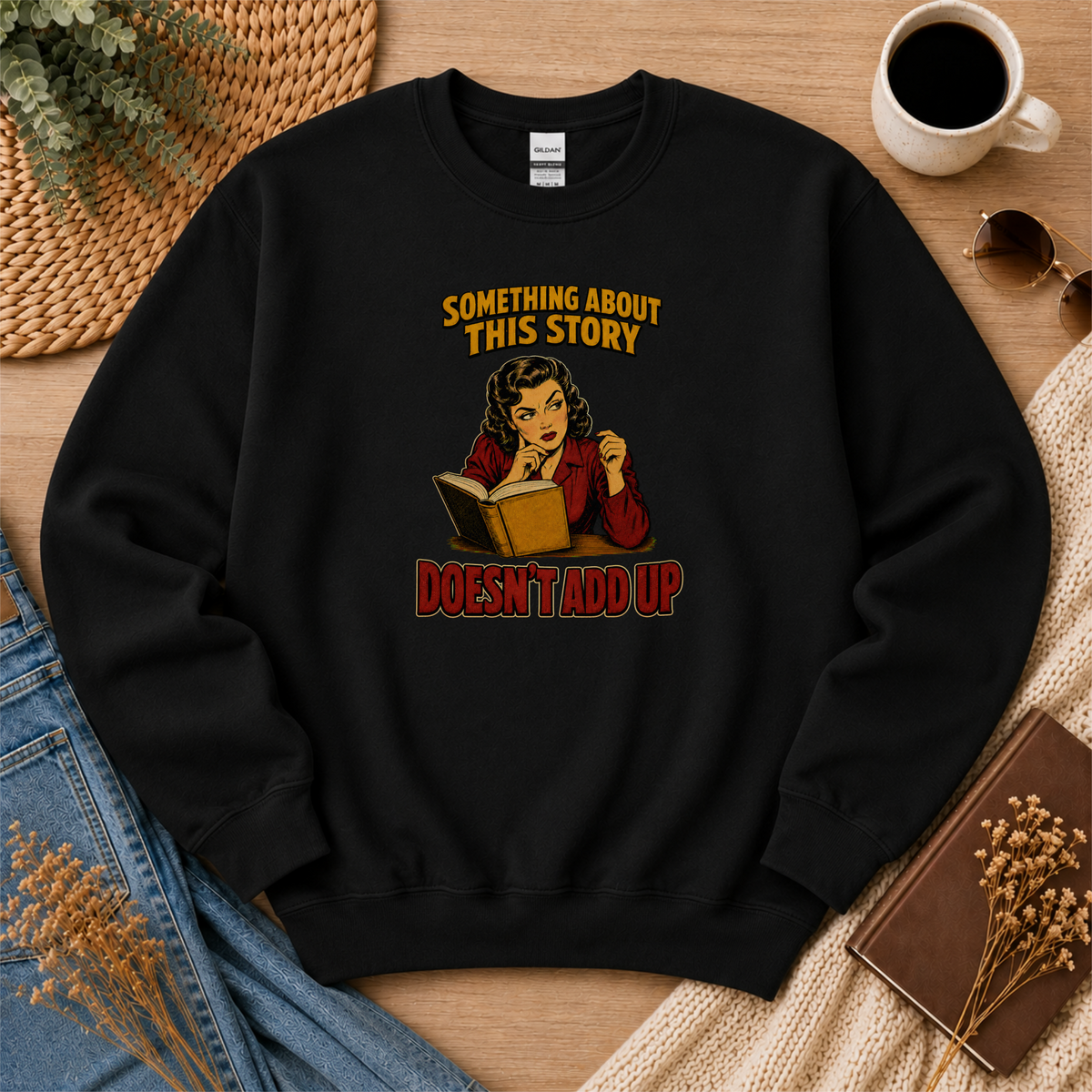 Black crewneck sweatshirt laid flat with an illustrated reader holding an open book and the words “Something About This Story Doesn’t Add Up.”