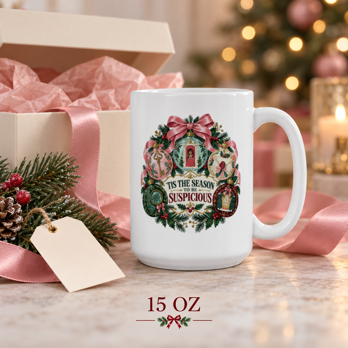 15-ounce “’Tis the Season to Be Suspicious” mug beside an open gift box with pink tissue and ribbon, evergreen branches, pinecone and blank gift tag.