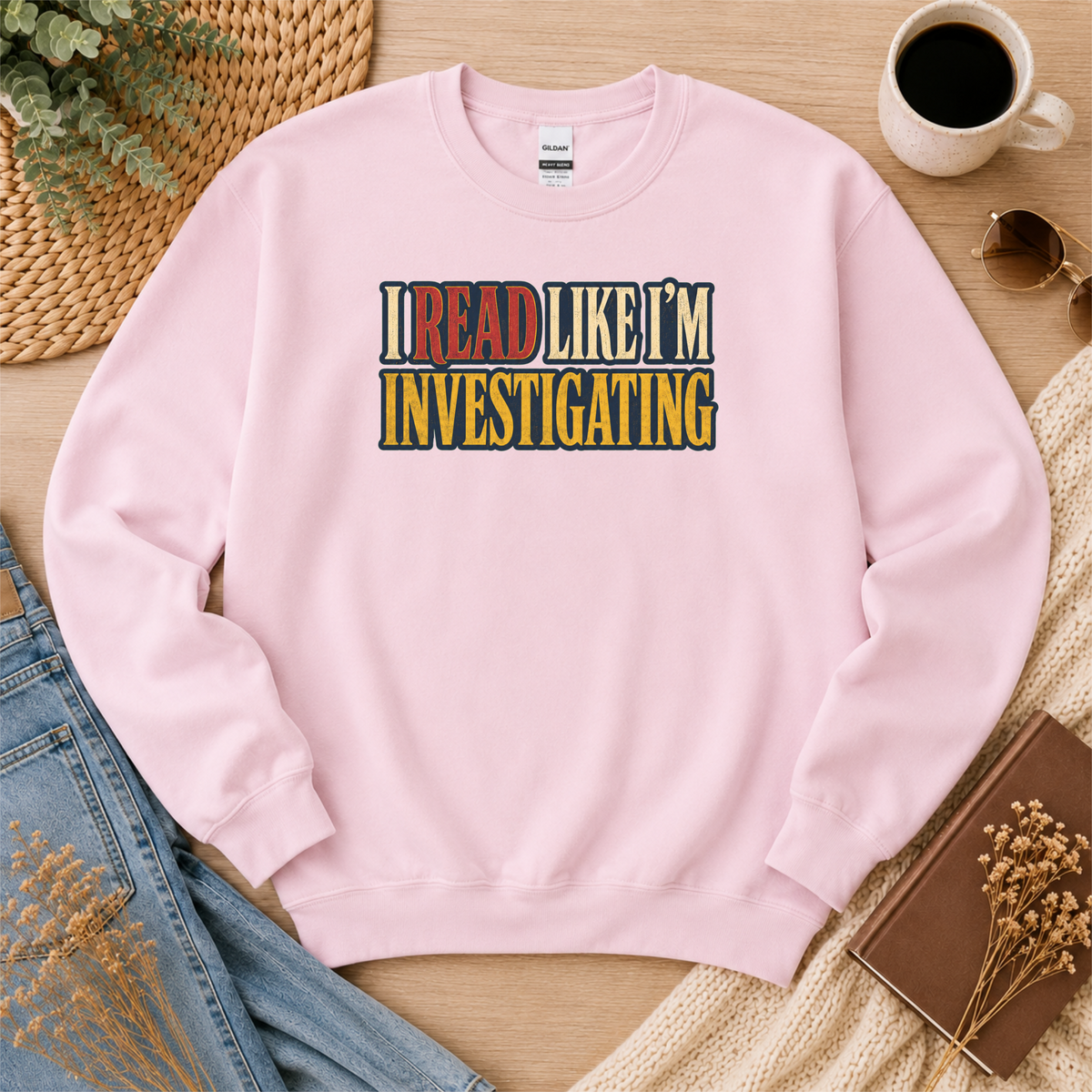 Light pink crewneck sweatshirt laid flat with bold vintage lettering and the words “I Read Like I’m Investigating.”