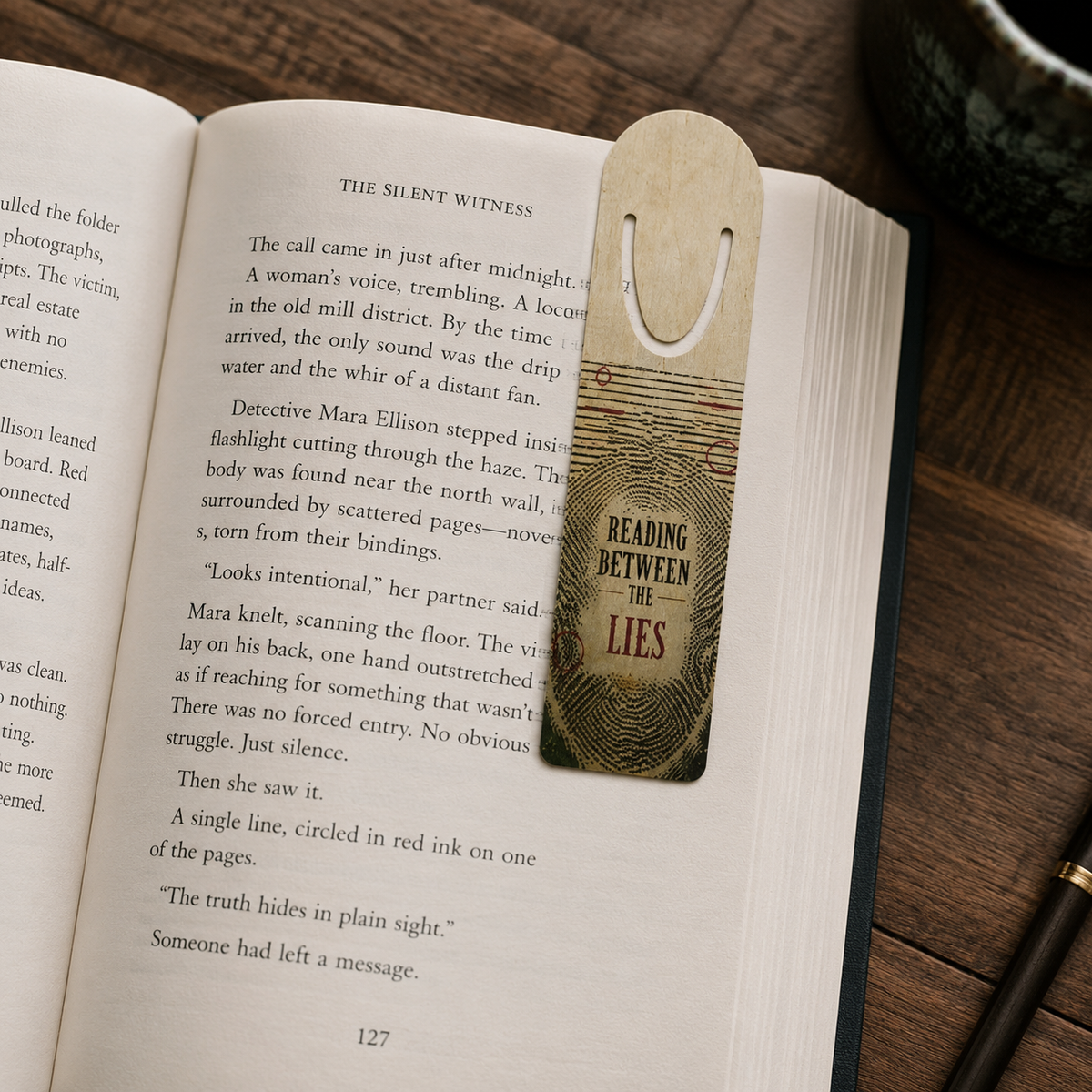 “Reading Between the Lies” aluminum bookmark with fingerprint-pattern lines clipped over a page in an open mystery novel.