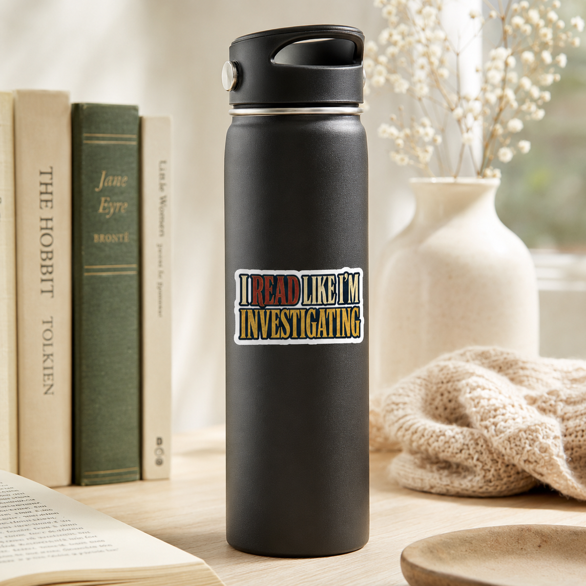 “I Read Like I’m Investigating” sticker with red, cream, and gold block lettering, shown on a black water bottle.