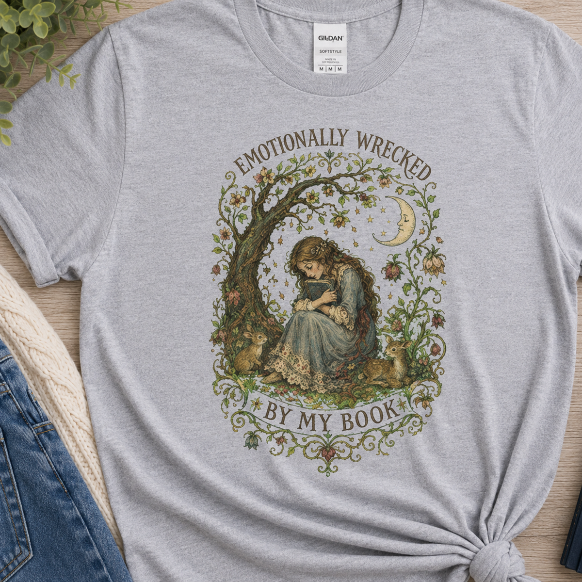Close-up of a sport gray T-shirt, showing the chest print with a reader beneath a tree, flowers and a crescent moon and the words “Emotionally Wrecked by My Book.”