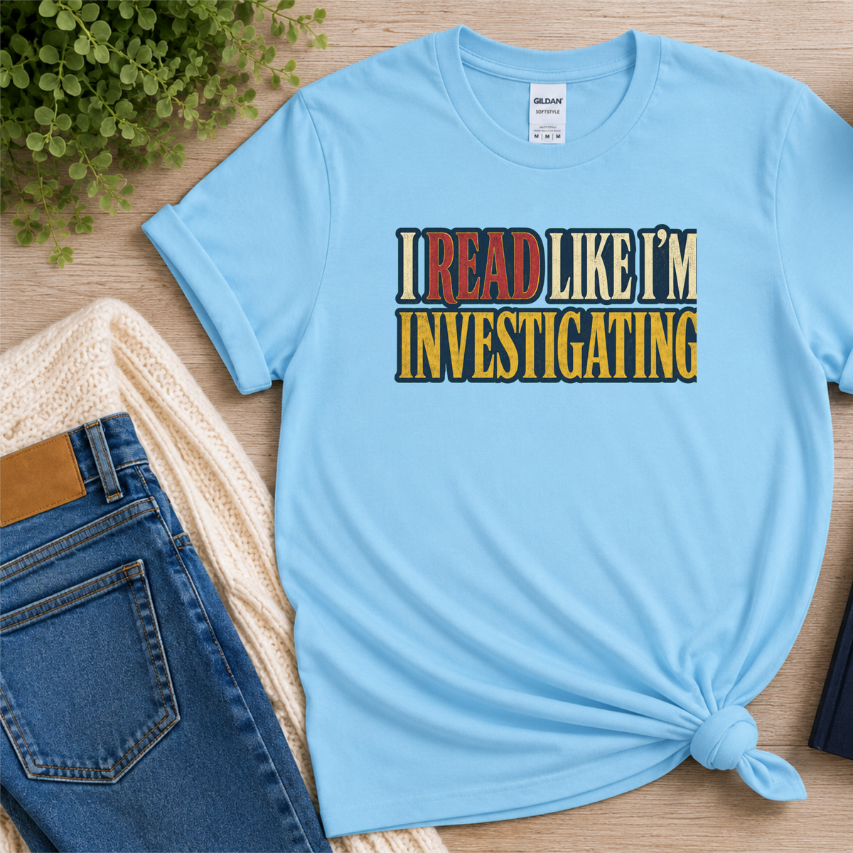 Light blue T-shirt laid flat with bold vintage lettering and the words “I Read Like I’m Investigating.”