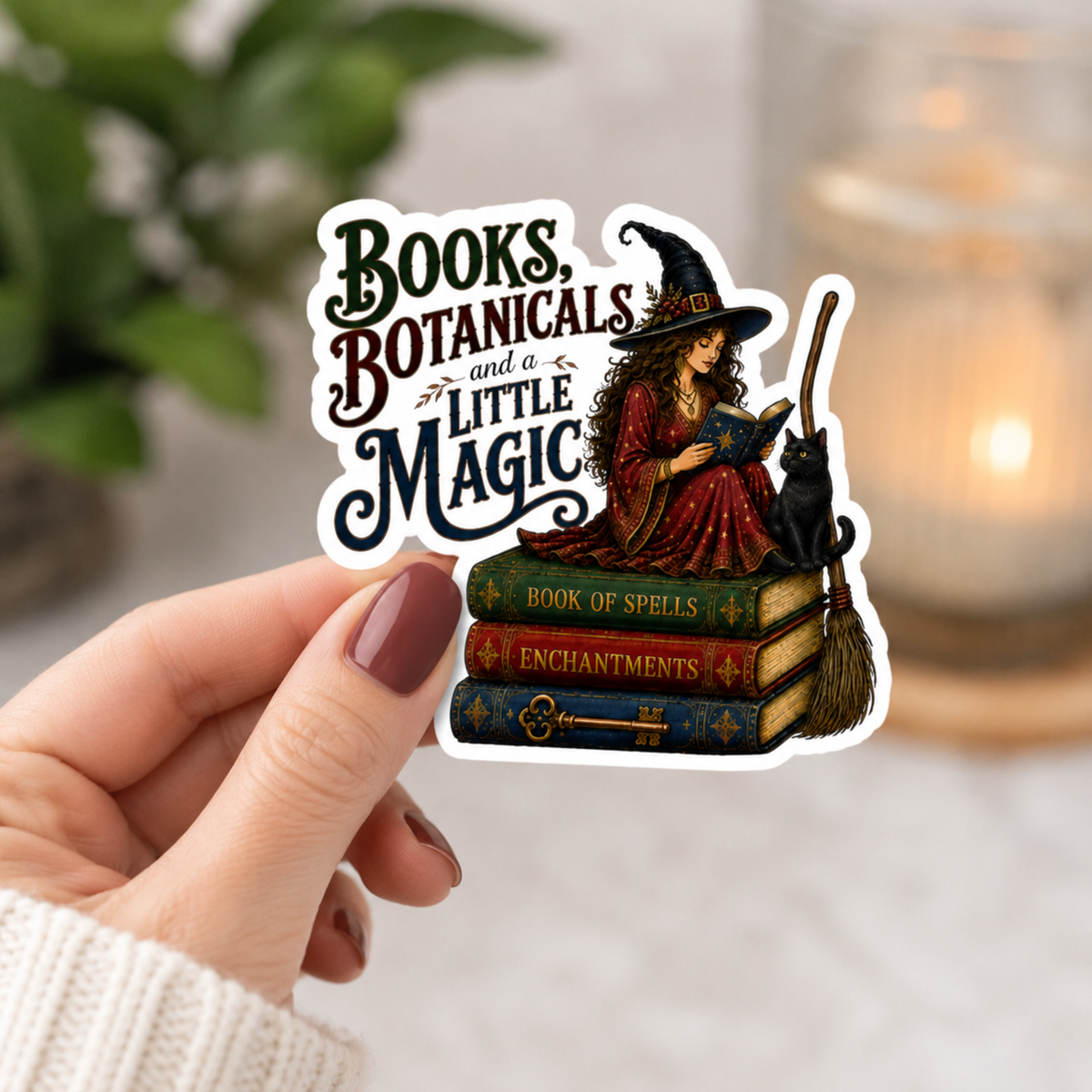 Hand holding a white-bordered sticker reading “Books, Botanicals and a Little Magic,” featuring a witch in a red dress reading beside a black cat, broom, and stacked spell books.