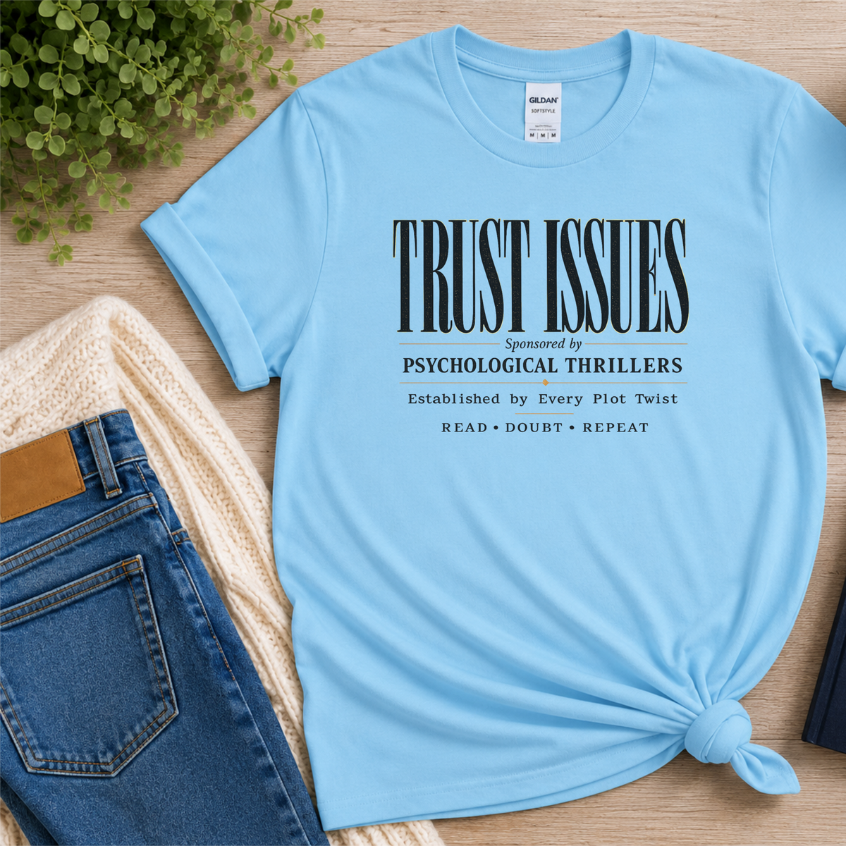 Light blue T-shirt laid flat with stacked typography and the words “Trust Issues. Sponsored by Psychological Thrillers. Established by Every Plot Twist. Read Doubt Repeat.”