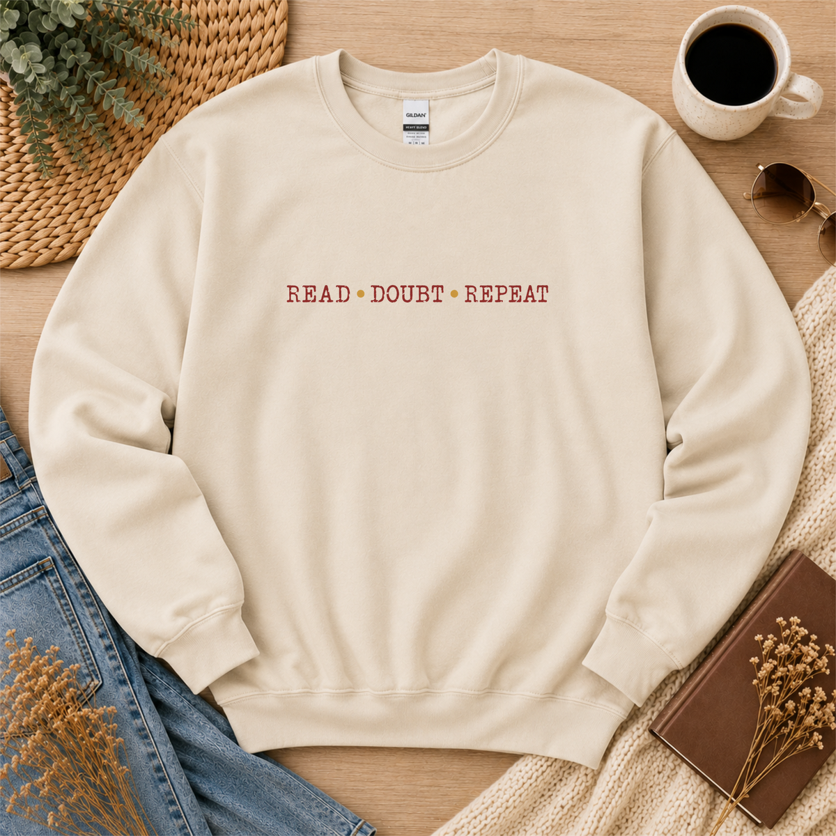 Sand crewneck sweatshirt laid flat with small red lettering across the chest and the words “Read Doubt Repeat.”