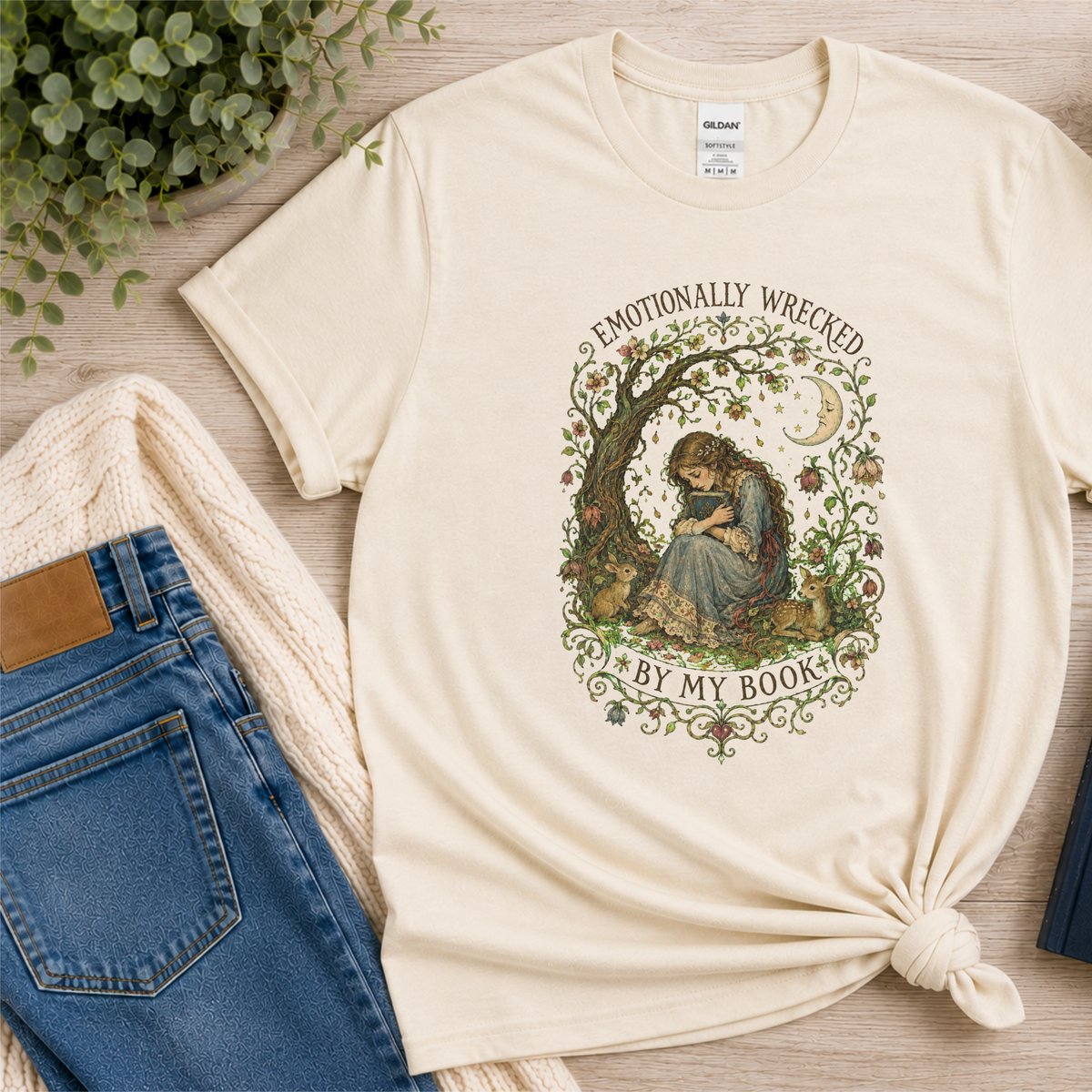 Natural cream T-shirt laid flat with a reader beneath a tree, flowers and a crescent moon and the words “Emotionally Wrecked by My Book.”