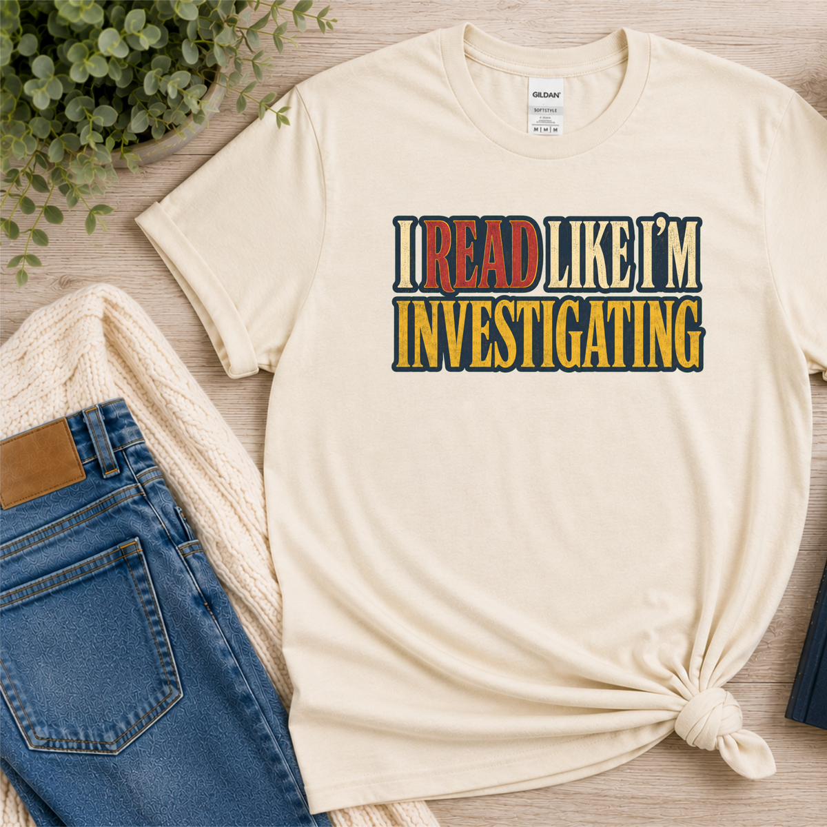 Natural cream T-shirt laid flat with bold vintage lettering and the words “I Read Like I’m Investigating.”