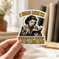 Hand holding a white-bordered sticker reading “I Read Like I’m Investigating,” featuring a retro reader taking notes while reading, framed by gold lettering.