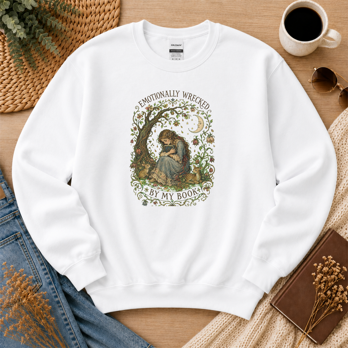 White crewneck sweatshirt laid flat with a reader beneath a tree, flowers and a crescent moon and the words “Emotionally Wrecked by My Book.”