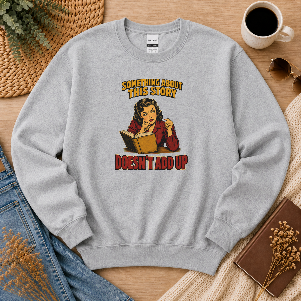 Sport gray crewneck sweatshirt laid flat with an illustrated reader holding an open book and the words “Something About This Story Doesn’t Add Up.”