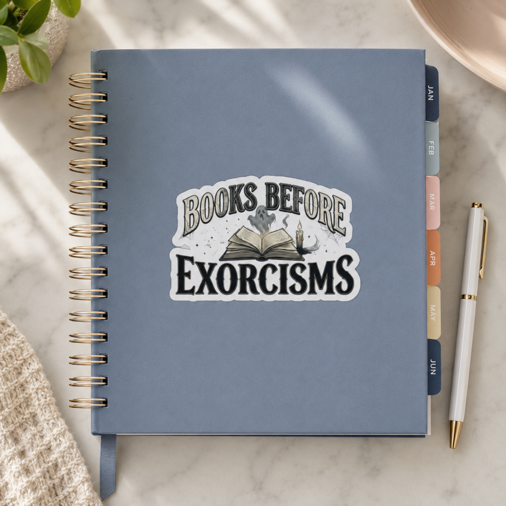 “Books Before Exorcisms” sticker with black lettering, an open book, gray ghost, candle, and cobweb, shown on a blue spiral planner.