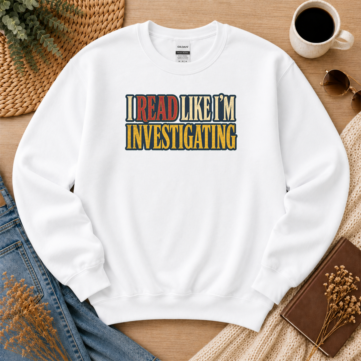 White crewneck sweatshirt laid flat with bold vintage lettering and the words “I Read Like I’m Investigating.”