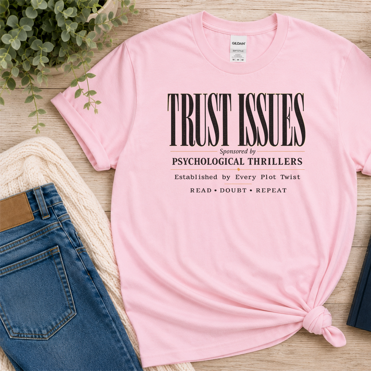 Light pink T-shirt laid flat with stacked typography and the words “Trust Issues. Sponsored by Psychological Thrillers. Established by Every Plot Twist. Read Doubt Repeat.”