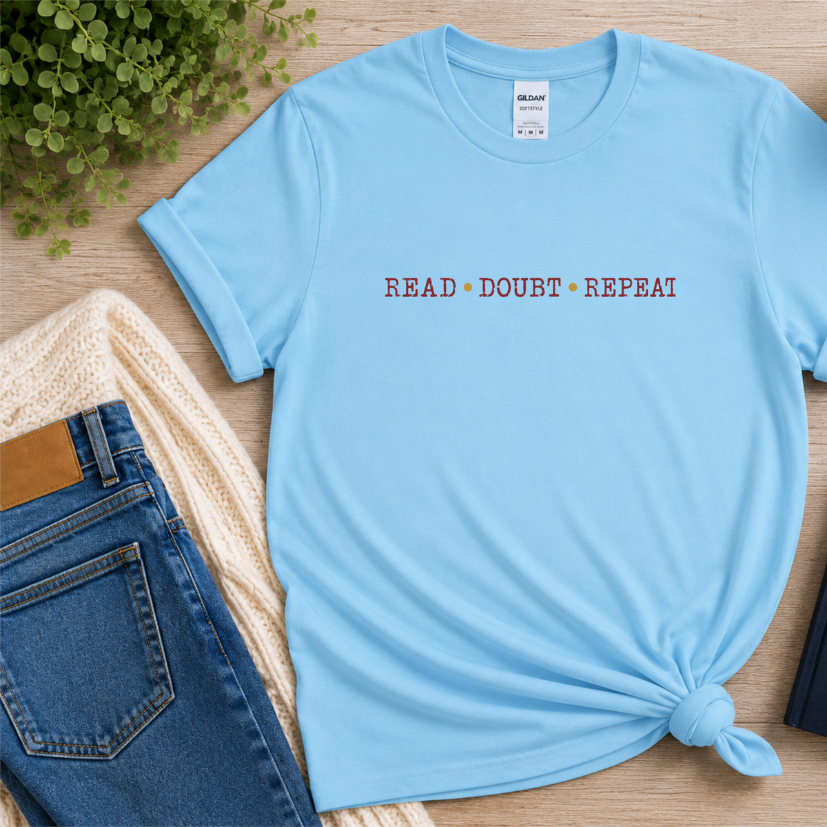 Light blue T-shirt laid flat with small red lettering across the chest and the words “Read Doubt Repeat.”