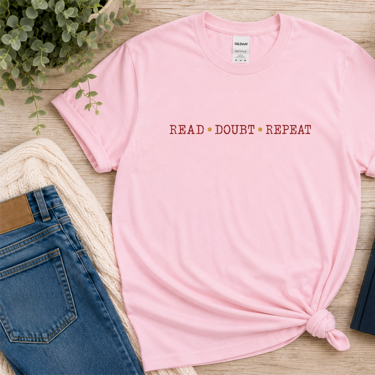 Light pink T-shirt laid flat with small red lettering across the chest and the words “Read Doubt Repeat.”