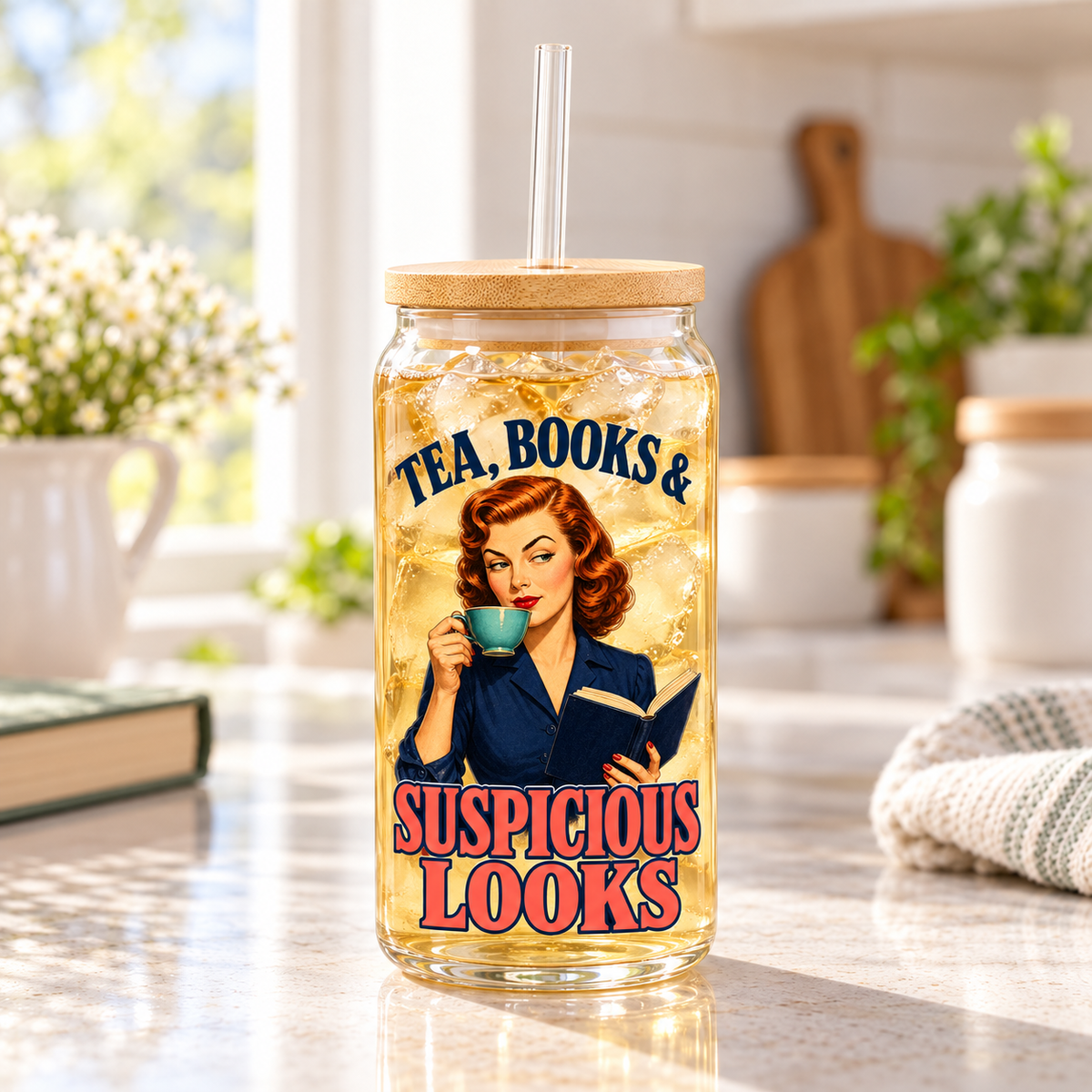 “Tea, Books & Suspicious Looks” glass sipper filled with light iced tea on a sunlit kitchen counter beside books and a towel; retro reader artwork, bamboo lid and clear straw.