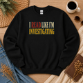 Black crewneck sweatshirt laid flat with bold vintage lettering and the words “I Read Like I’m Investigating.”