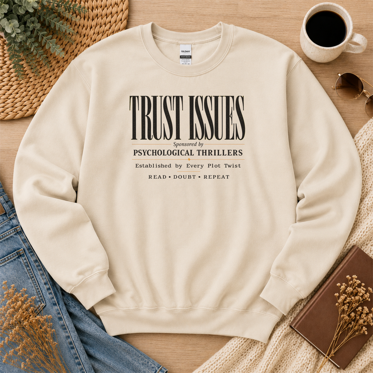 Sand crewneck sweatshirt laid flat with stacked typography and the words “Trust Issues. Sponsored by Psychological Thrillers. Established by Every Plot Twist. Read Doubt Repeat.”