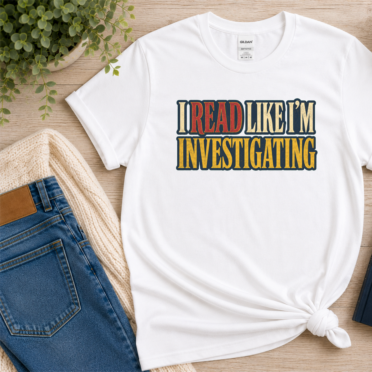 White T-shirt laid flat with bold vintage lettering and the words “I Read Like I’m Investigating.”