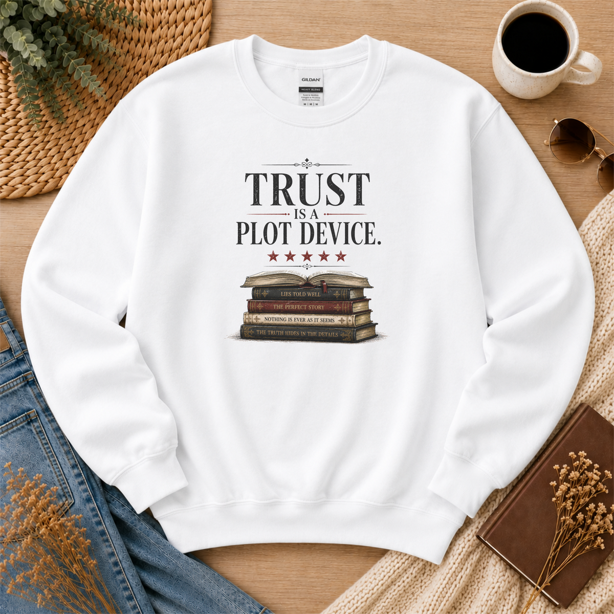 White crewneck sweatshirt laid flat with stars above a stack of books and the words “Trust Is a Plot Device.”