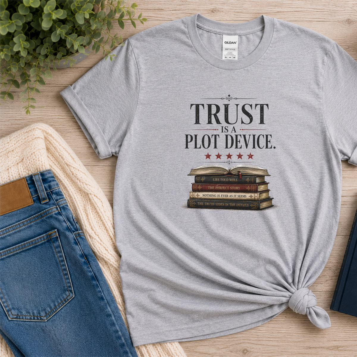 Sport gray T-shirt laid flat with stars above a stack of books and the words “Trust Is a Plot Device.”