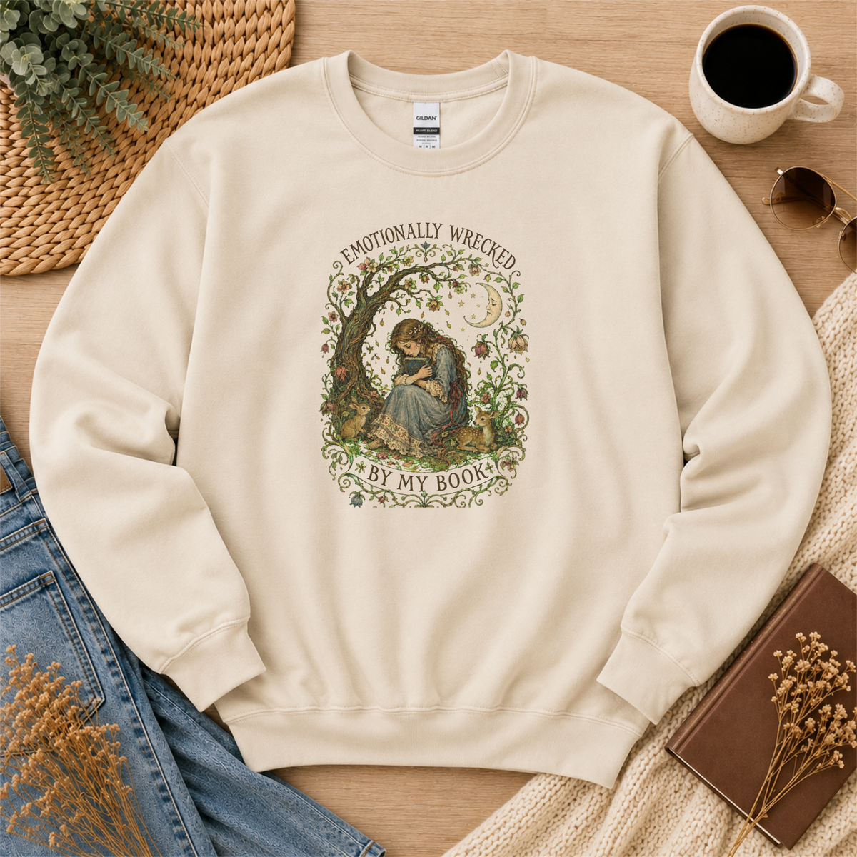 Sand crewneck sweatshirt laid flat with a reader beneath a tree, flowers and a crescent moon and the words “Emotionally Wrecked by My Book.”