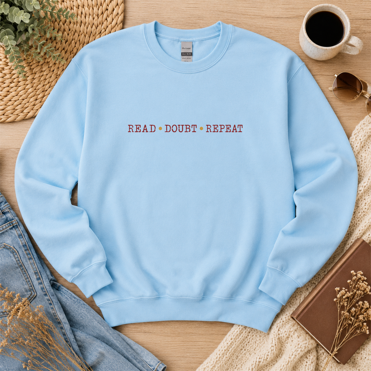 Light blue crewneck sweatshirt laid flat with small red lettering across the chest and the words “Read Doubt Repeat.”