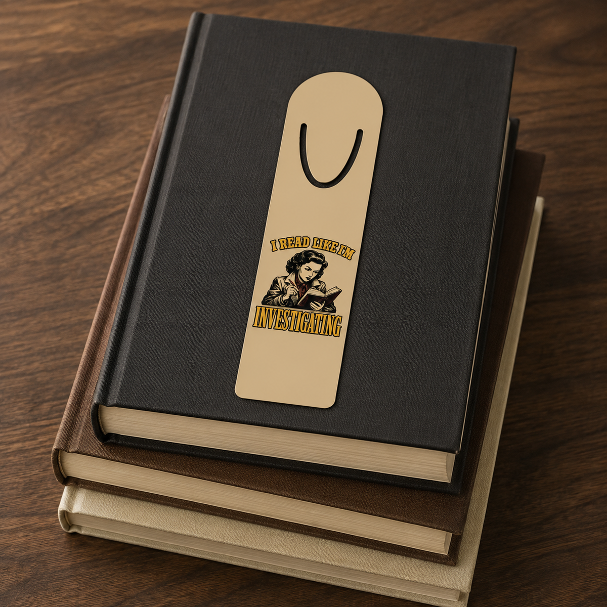I Read Like I’m Investigating aluminum bookmark displayed on a stack of three closed hardcover books.