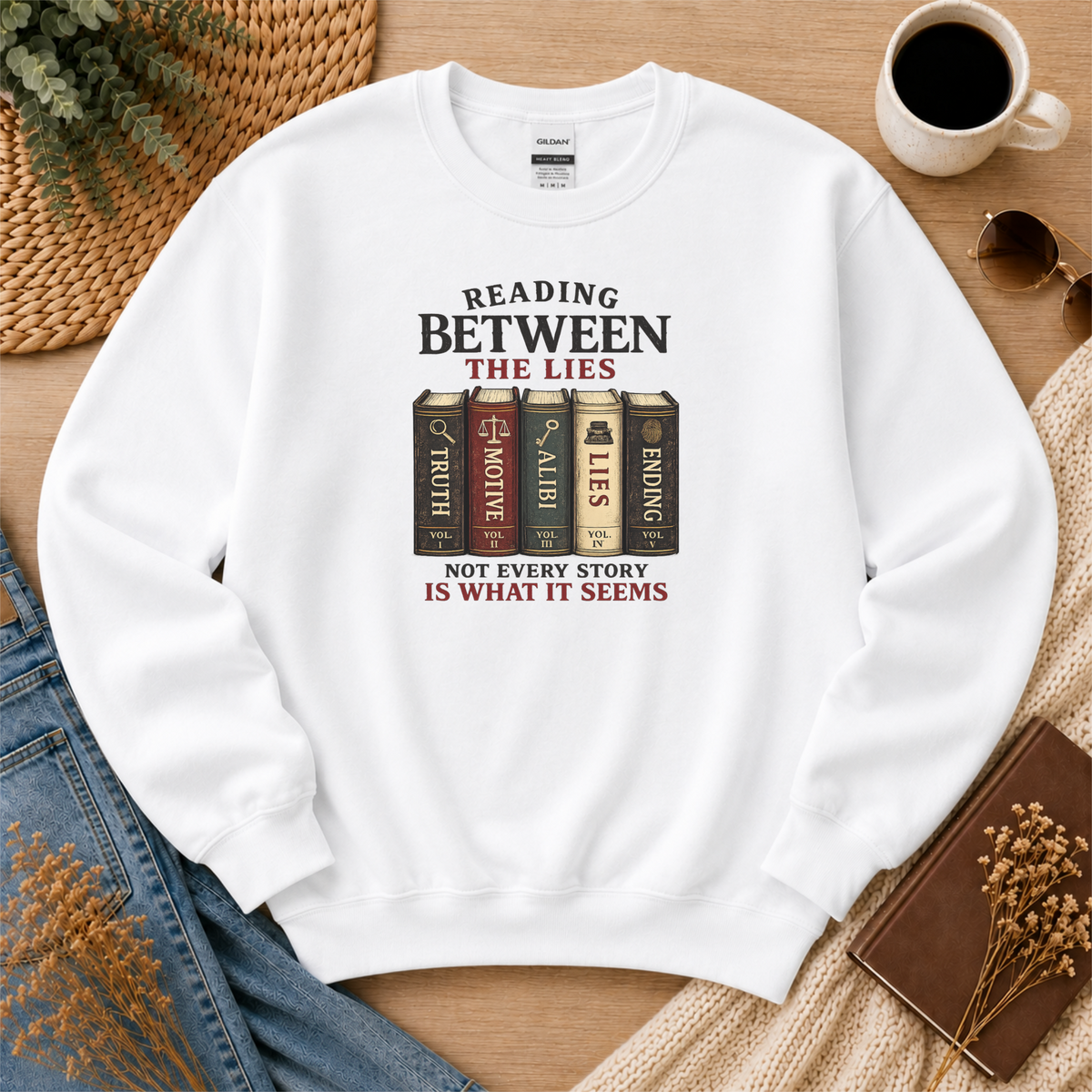 White crewneck sweatshirt laid flat with books labeled Truth, Motive, Alibi, Lies and Ending and the words “Reading Between the Lies. Not Every Story Is What It Seems.”
