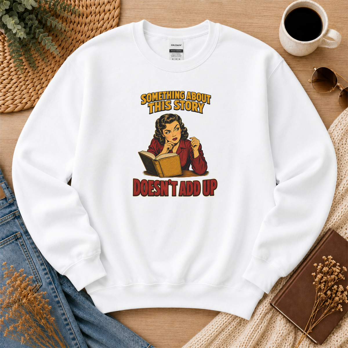 White crewneck sweatshirt laid flat with an illustrated reader holding an open book and the words “Something About This Story Doesn’t Add Up.”