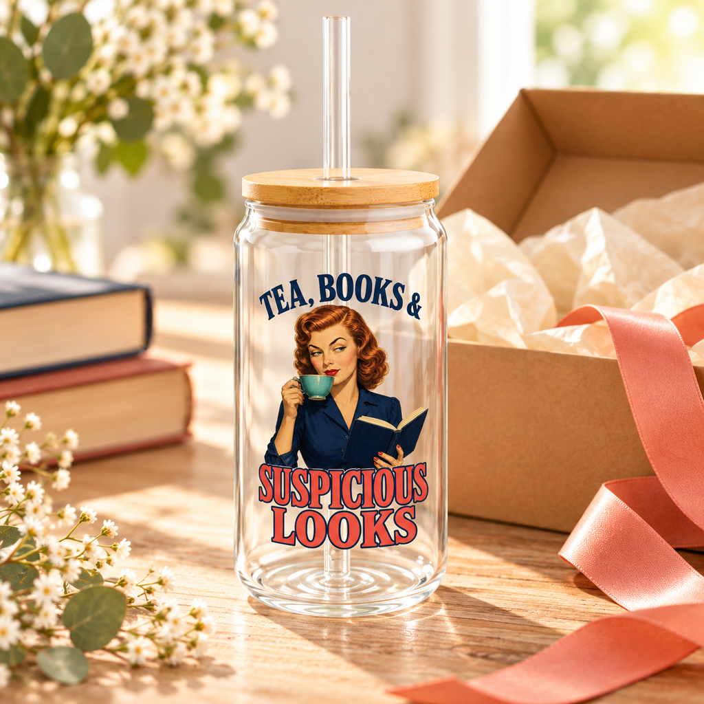 Empty “Tea, Books & Suspicious Looks” glass sipper with a retro red-haired reader, bamboo lid and clear straw beside a tissue-lined gift box, coral ribbon and books.