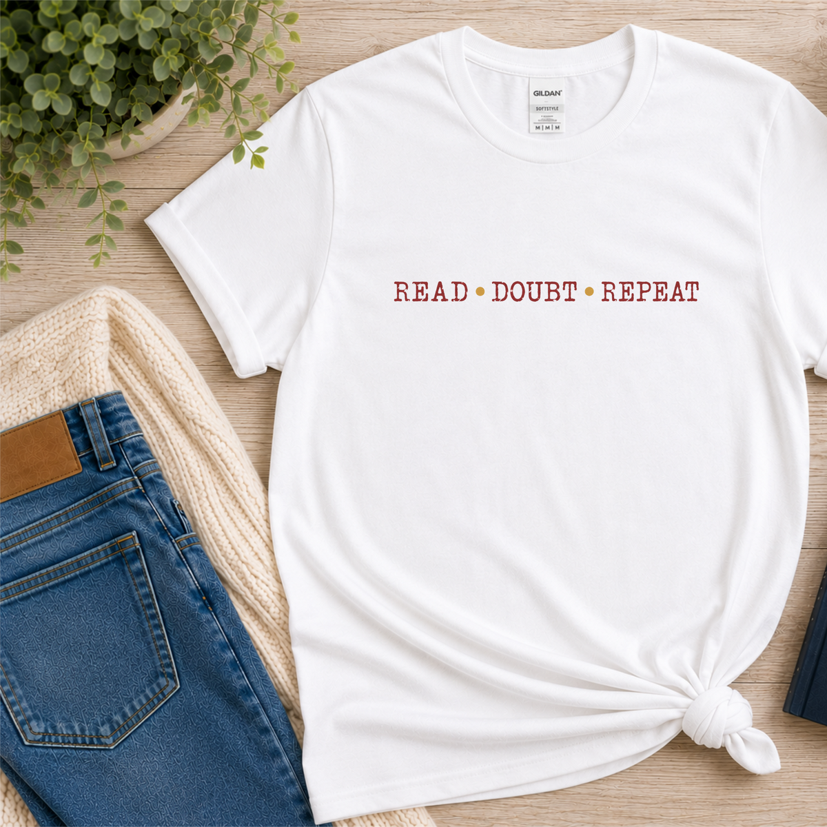 White T-shirt laid flat with small red lettering across the chest and the words “Read Doubt Repeat.”