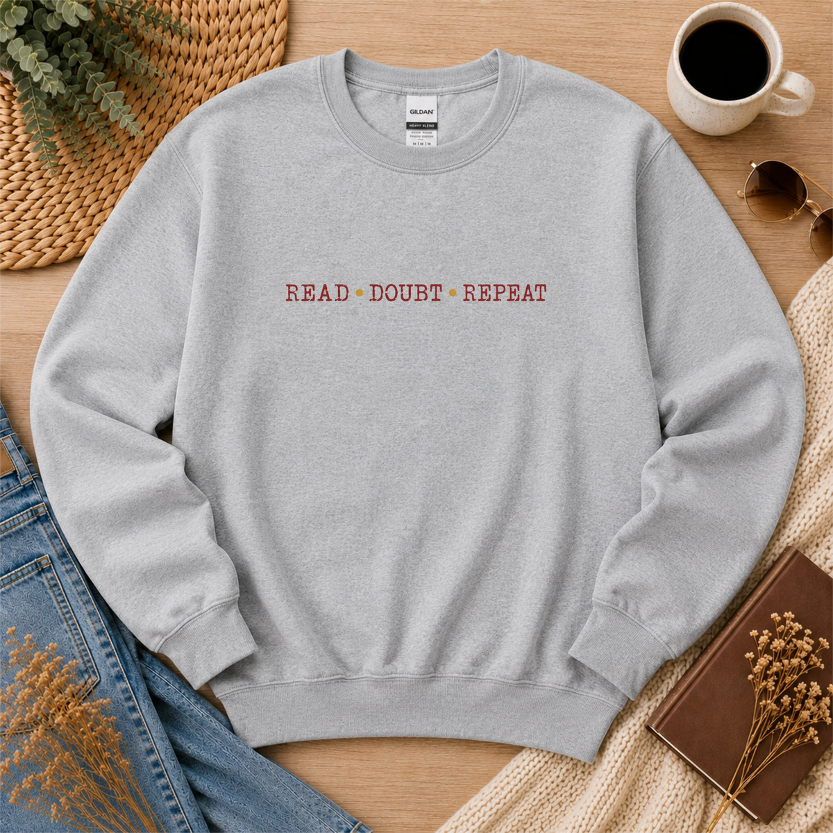 Sport gray crewneck sweatshirt laid flat with small red lettering across the chest and the words “Read Doubt Repeat.”