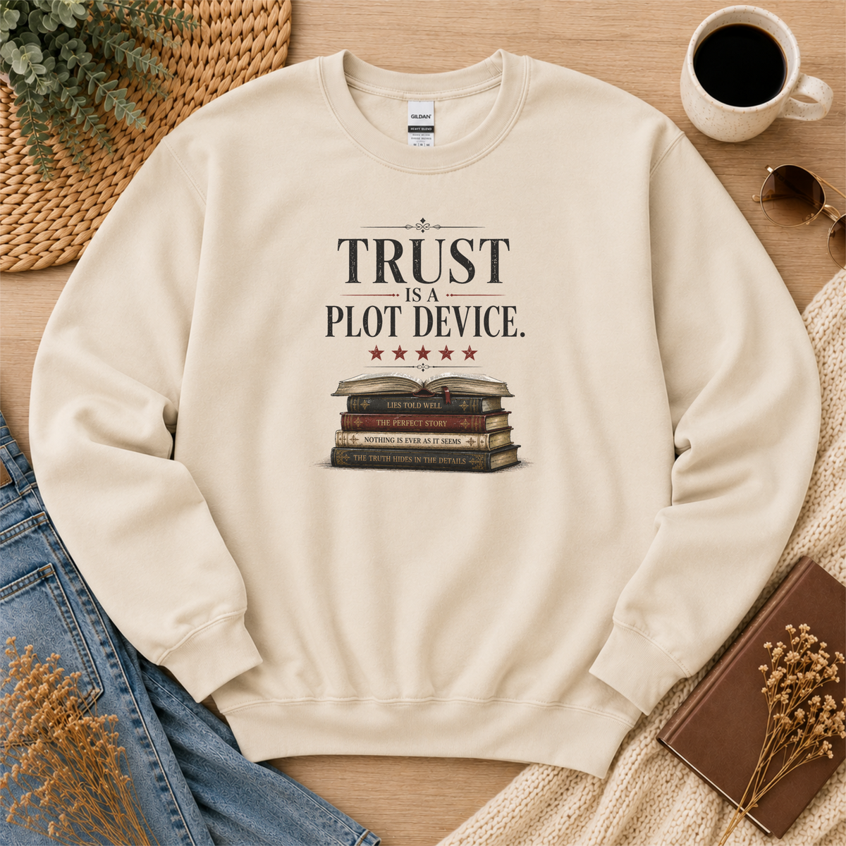 Sand crewneck sweatshirt laid flat with stars above a stack of books and the words “Trust Is a Plot Device.”