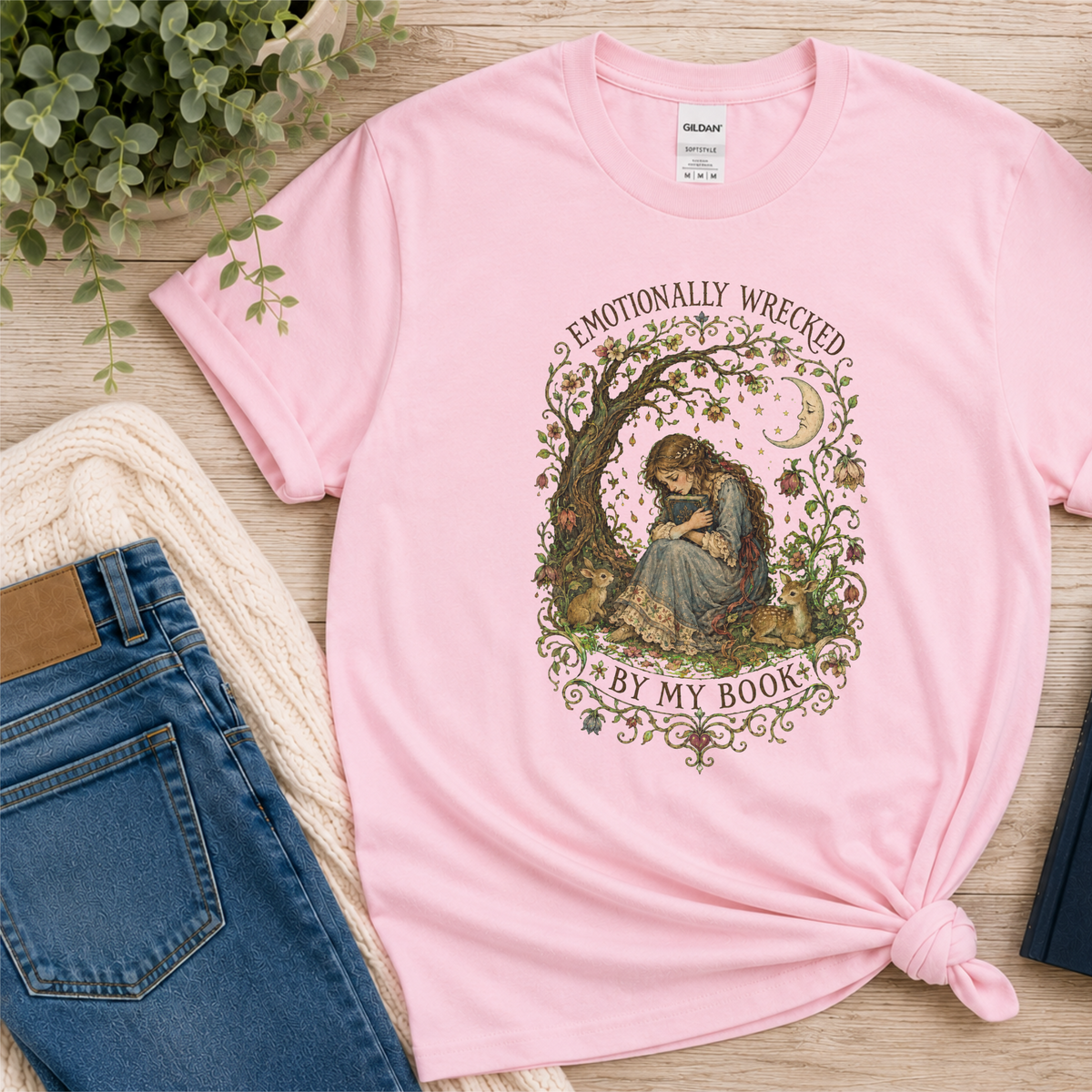 Light pink T-shirt laid flat with a reader beneath a tree, flowers and a crescent moon and the words “Emotionally Wrecked by My Book.”