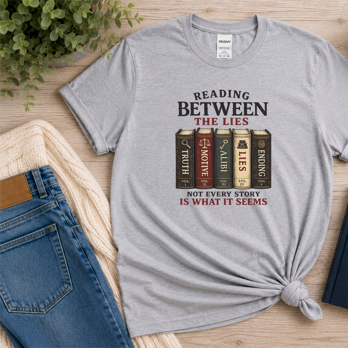 Sport gray T-shirt laid flat with books labeled Truth, Motive, Alibi, Lies and Ending and the words “Reading Between the Lies. Not Every Story Is What It Seems.”