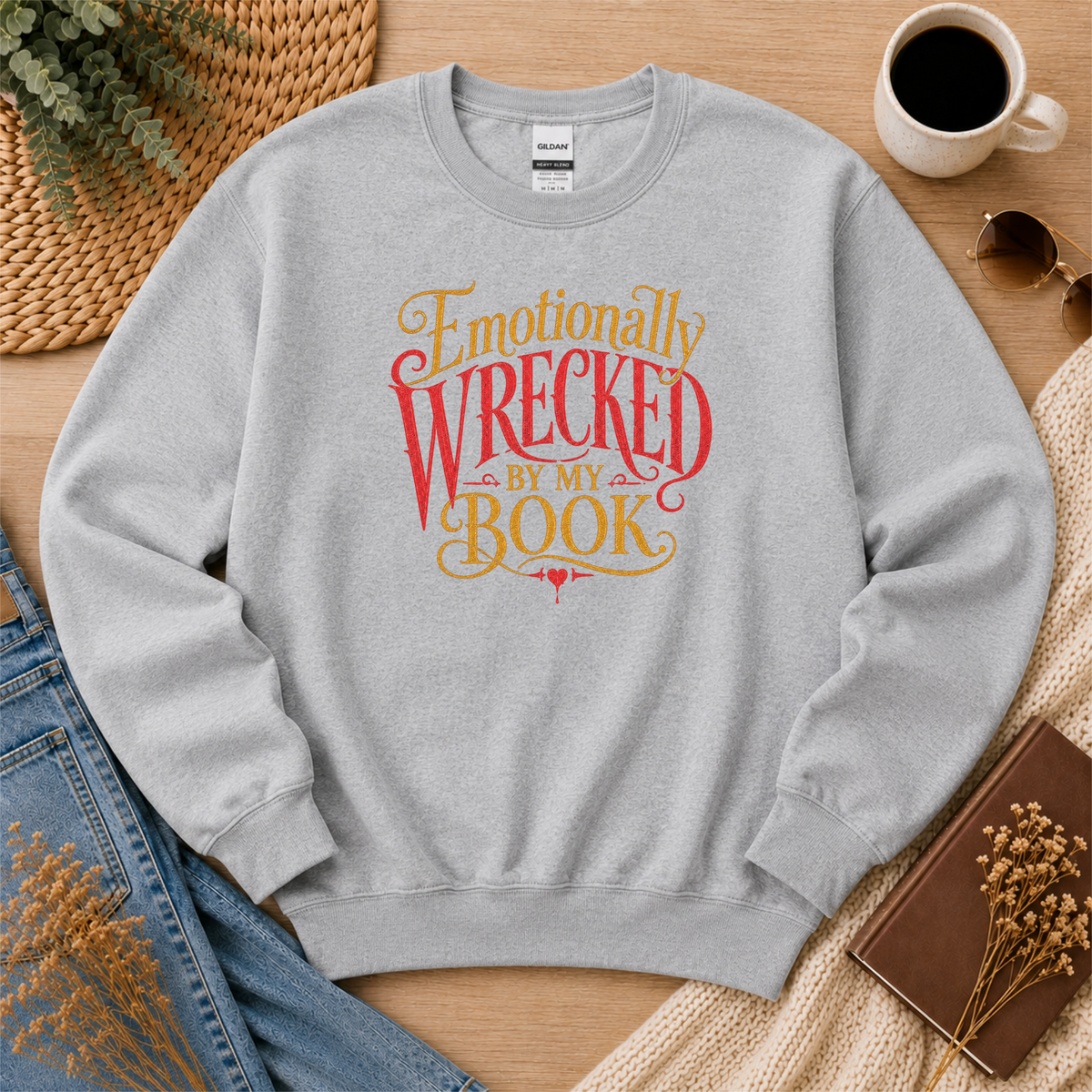 Sport gray crewneck sweatshirt laid flat with ornate red and gold lettering and the words “Emotionally Wrecked by My Book.”