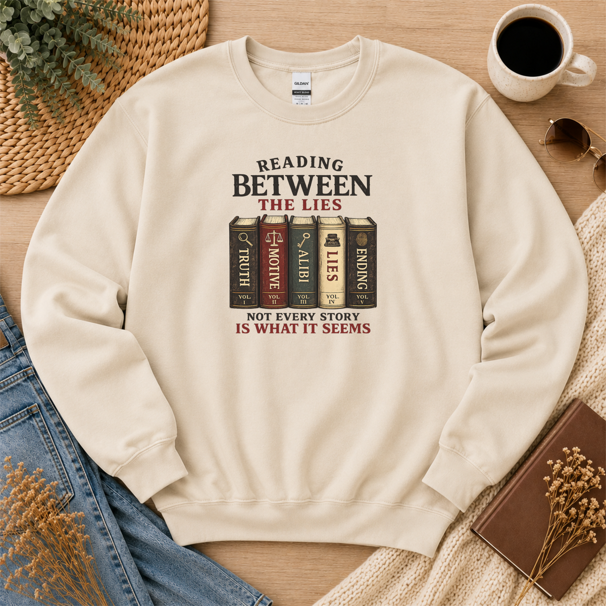 Sand crewneck sweatshirt laid flat with books labeled Truth, Motive, Alibi, Lies and Ending and the words “Reading Between the Lies. Not Every Story Is What It Seems.”