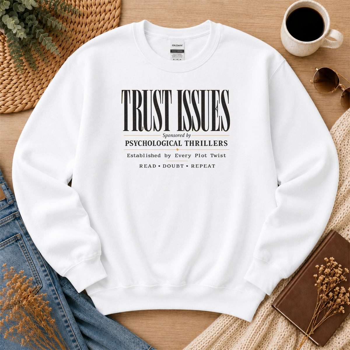 White crewneck sweatshirt laid flat with stacked typography and the words “Trust Issues. Sponsored by Psychological Thrillers. Established by Every Plot Twist. Read Doubt Repeat.”