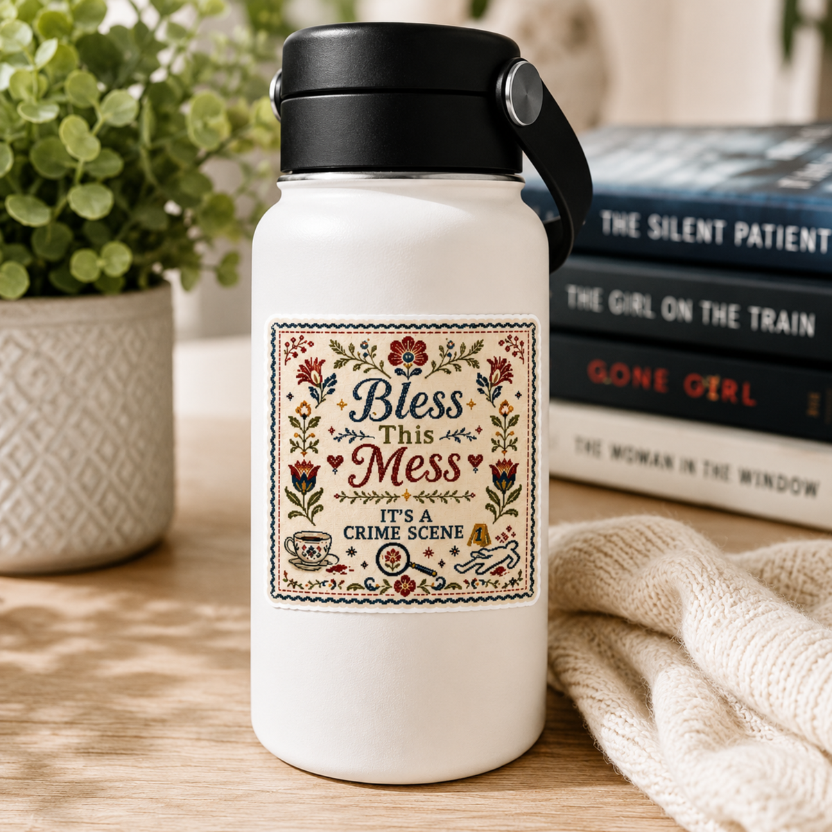 “Bless This Mess. It’s a Crime Scene” sticker with a folk-art floral border, teacup, magnifying glass, evidence marker, and body outline, shown on a white water bottle.