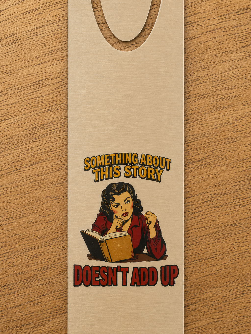 Close-up of the gold-tone aluminum bookmark showing a reader studying an open book beneath the words “Something About This Story Doesn’t Add Up.”