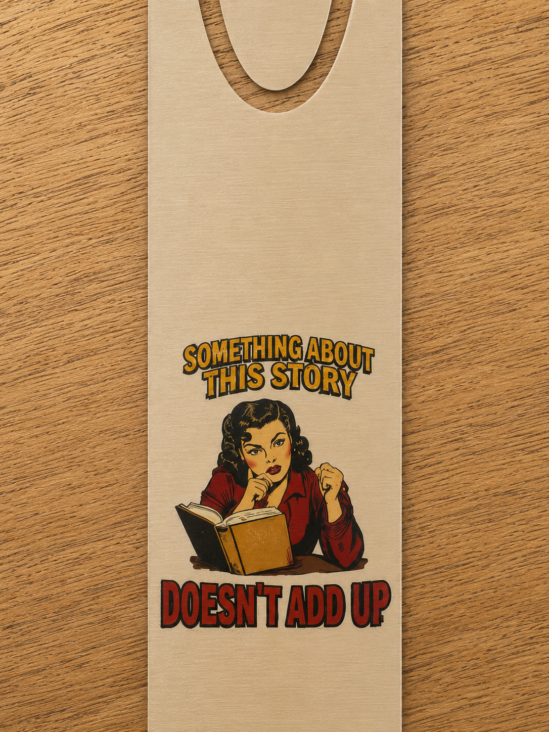 Close-up of the gold-tone aluminum bookmark showing a reader studying an open book beneath the words “Something About This Story Doesn’t Add Up.”